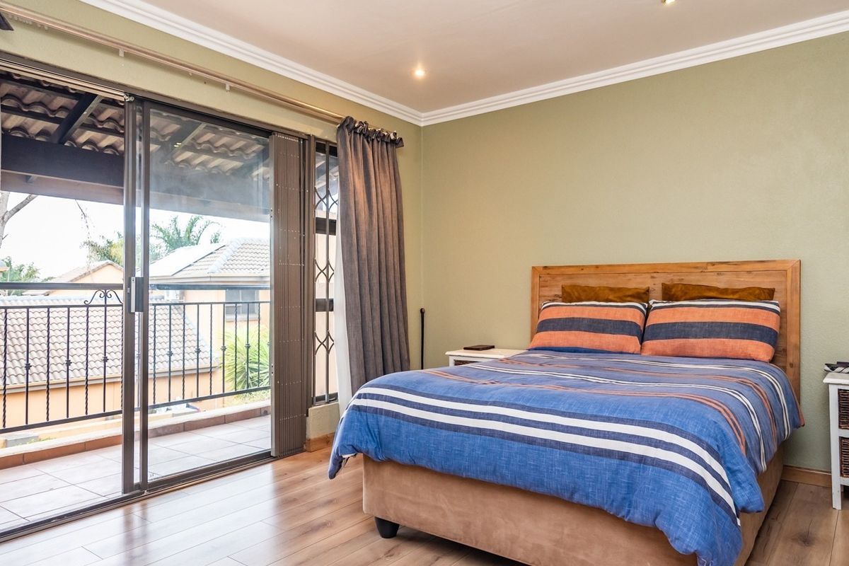 A well-maintained bedroom featuring laminate flooring, crown molding, and a large sliding glass door providing access to a private balcony.