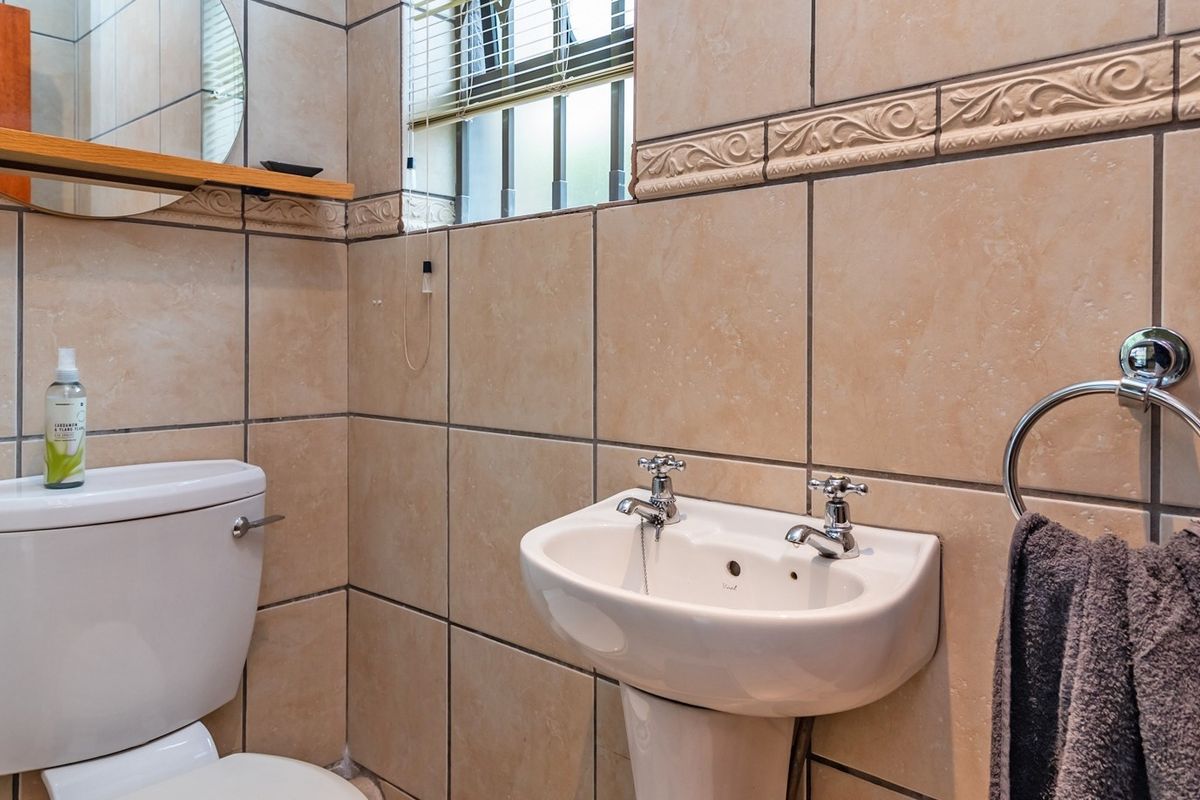A functional bathroom featuring a pedestal basin with dual taps, a standard toilet, and neutral ceramic wall tiling with decorative border accents.