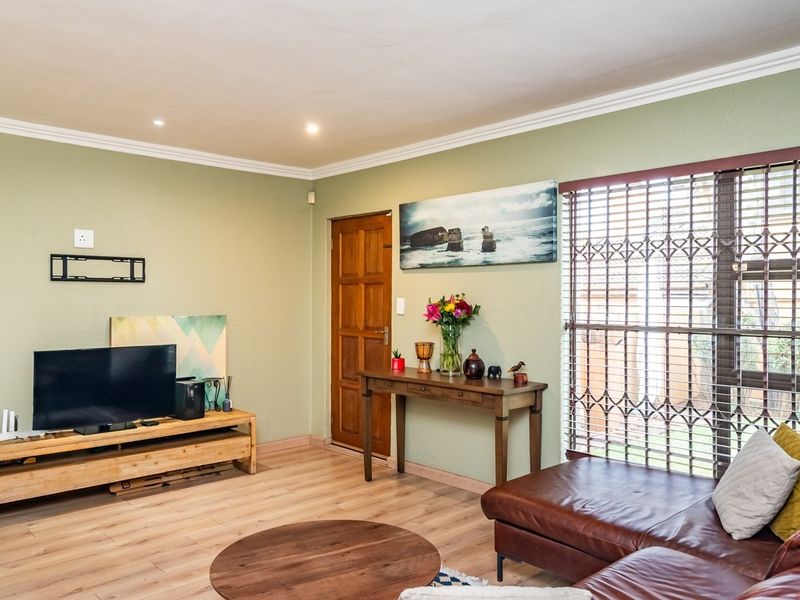 A well-lit living room featuring laminate flooring, decorative cornicing, and a secure entrance with a fitted security gate.