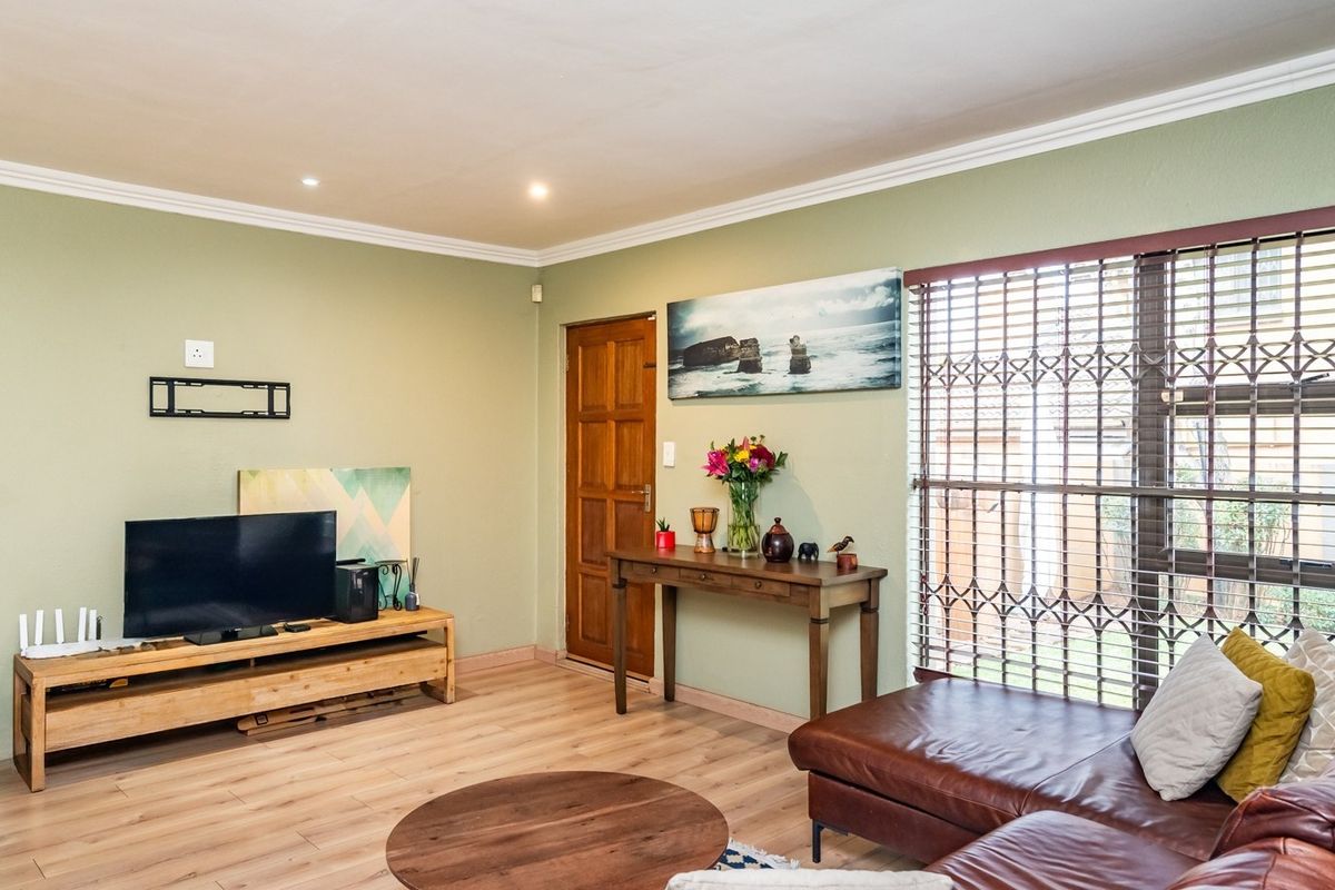 A well-lit living room featuring laminate flooring, decorative cornicing, and a secure entrance with a fitted security gate.