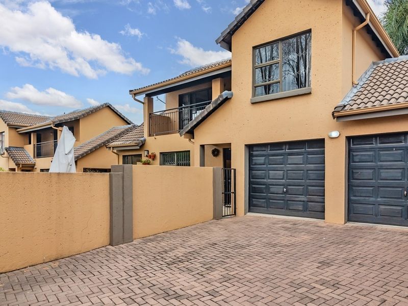 Front view of a double-story townhouse featuring a paved driveway, double garage, and a balcony, showcasing the property's exterior facade and entrance.