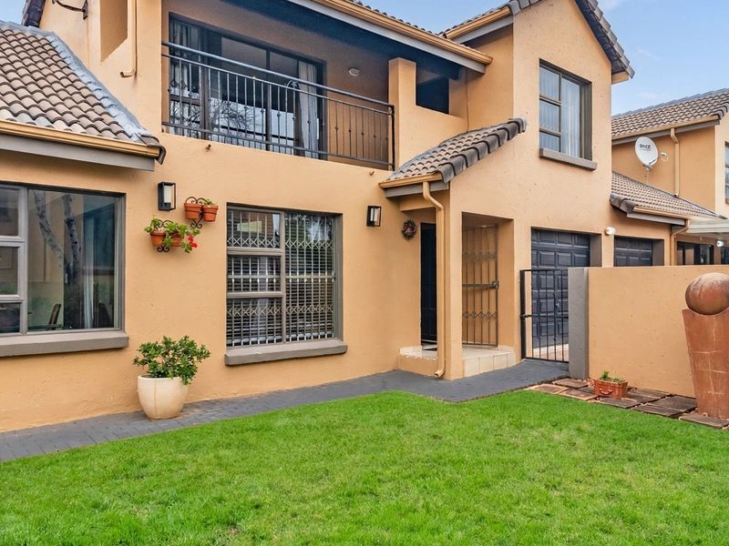 Front view of a townhouse featuring a paved walkway, small lawn, balcony with metal railing, and secure garage access.