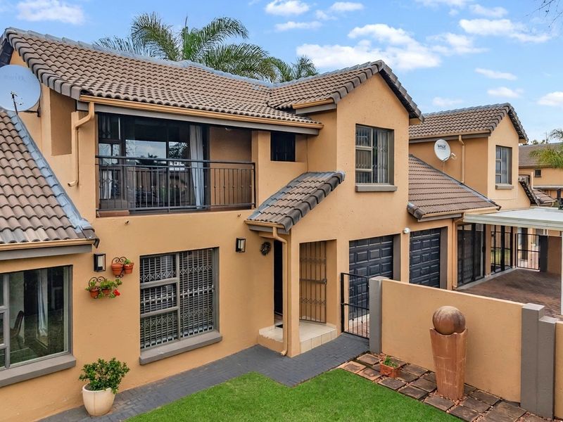 A well-maintained double-story townhouse featuring a tiled roof, balcony, paved driveway, and secure garage access within a residential complex.