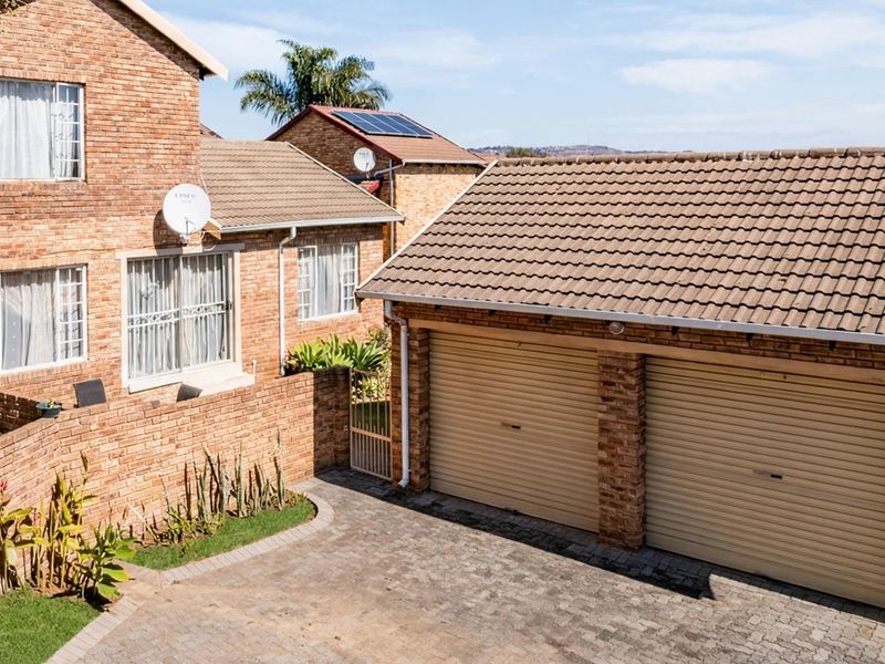 An elevated view of a face brick townhouse featuring a double garage, paved driveway, and solar panels on the roof.
