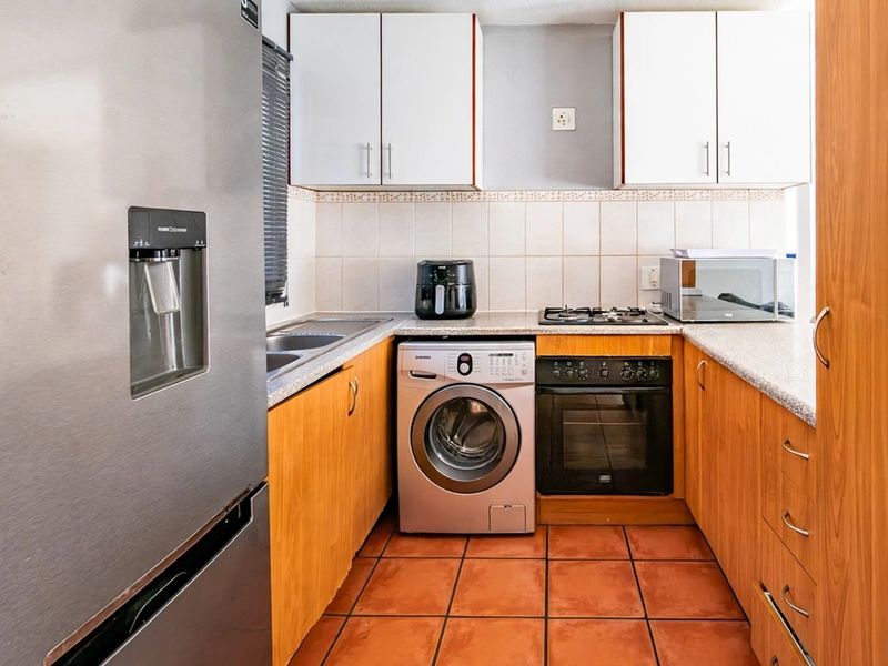 A functional kitchen featuring wood-finish cabinetry, tiled backsplash, gas hob, built-in oven, and tiled flooring, providing a practical workspace.
