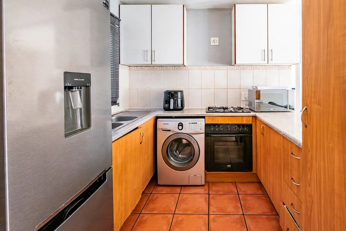 A functional kitchen featuring wood-finish cabinetry, tiled backsplash, gas hob, built-in oven, and tiled flooring, providing a practical workspace.