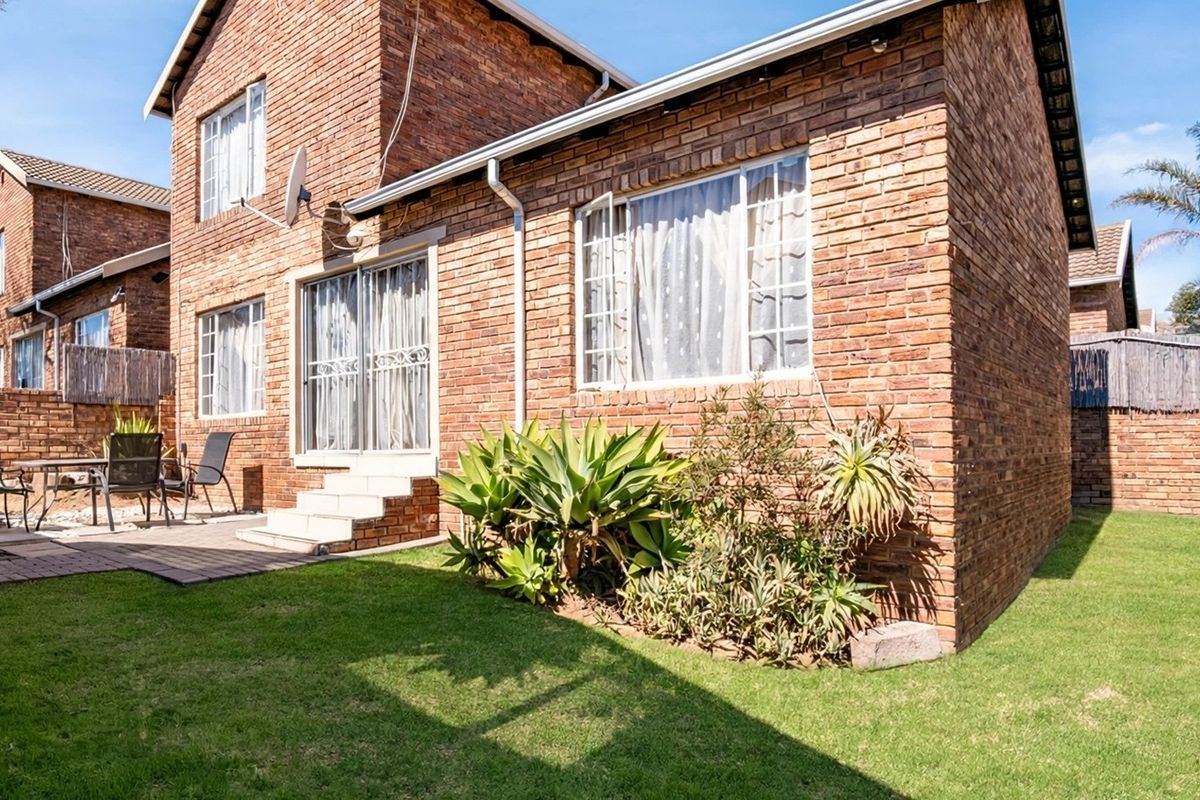 Rear view of a face brick townhouse featuring a paved patio area, well-maintained lawn, and sliding door access to the interior.