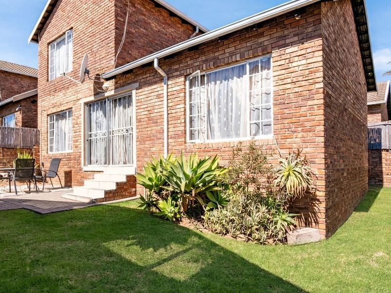Rear view of a face brick townhouse featuring a paved patio area, well-maintained lawn, and sliding door access to the interior.