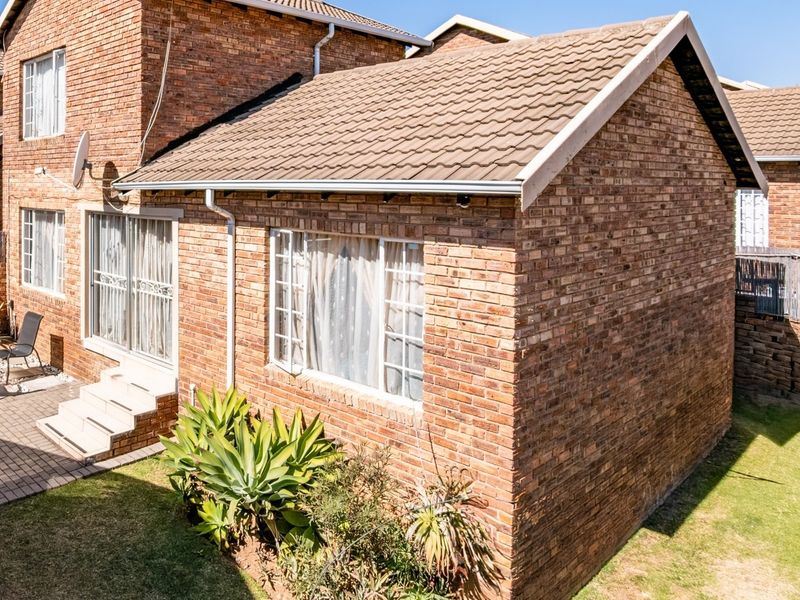 Rear view of a face brick townhouse featuring a paved patio area, tiled roof, and sliding door access to the interior.