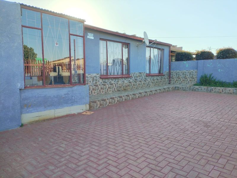 Front exterior view of the property featuring a paved driveway, stone-clad facade, and security bars on the windows.