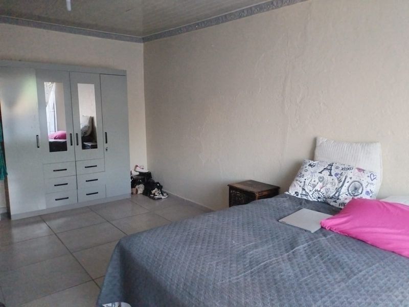 A bedroom featuring tiled flooring, a built-in wardrobe with mirrored panels, and coved ceiling detailing. The walls show signs of surface wear and plaster cracking.
