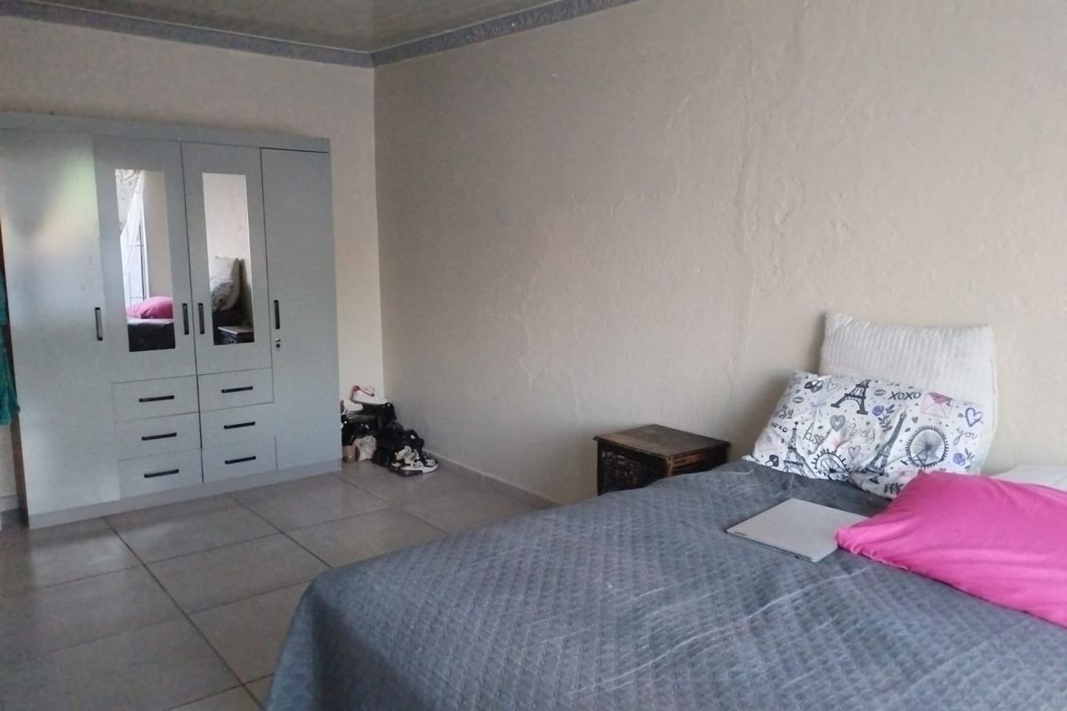 A bedroom featuring tiled flooring, a built-in wardrobe with mirrored panels, and coved ceiling detailing. The walls show signs of surface wear and plaster cracking.
