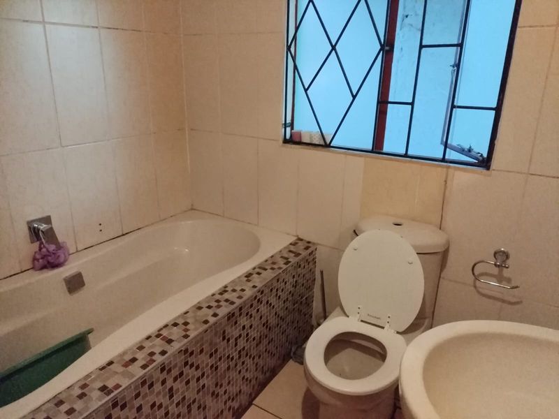A functional bathroom featuring a bathtub with mosaic tile surround, a standard toilet, and a pedestal basin, requiring cosmetic updates to modernize the space.