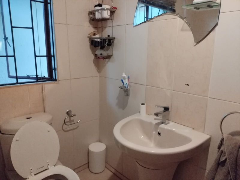 A compact bathroom featuring a pedestal basin, toilet, and tiled walls, with a window fitted with security bars.