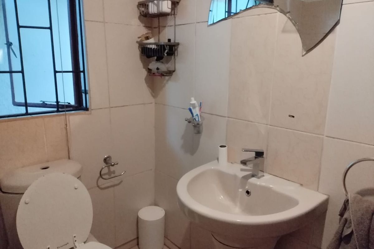 A compact bathroom featuring a pedestal basin, toilet, and tiled walls, with a window fitted with security bars.
