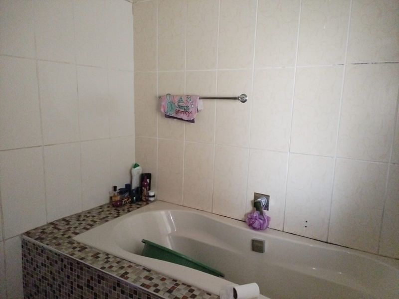 A bathroom featuring a built-in bathtub with a mosaic tile surround and neutral wall tiling.