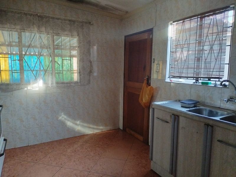 A dated kitchen featuring tiled walls, tiled flooring, and built-in cabinetry with a stainless steel sink and window security bars.