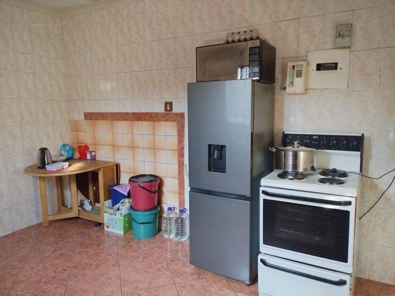 A functional kitchen area featuring tiled walls and flooring, equipped with a freestanding stove and integrated electrical distribution board.