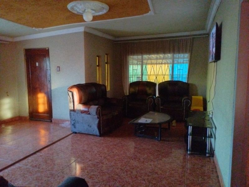 A living room featuring tiled flooring, a ceiling rose, and window security bars, offering a functional space with potential for cosmetic updates.
