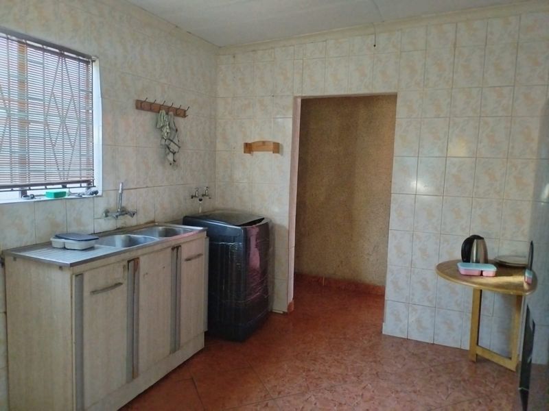 A functional laundry area featuring tiled walls, a double stainless steel sink, and dedicated plumbing connections for appliances.