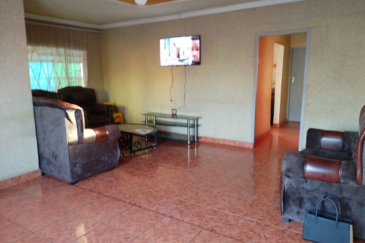 A living room featuring tiled flooring, coved ceilings with a central rose, and access to an adjacent hallway.