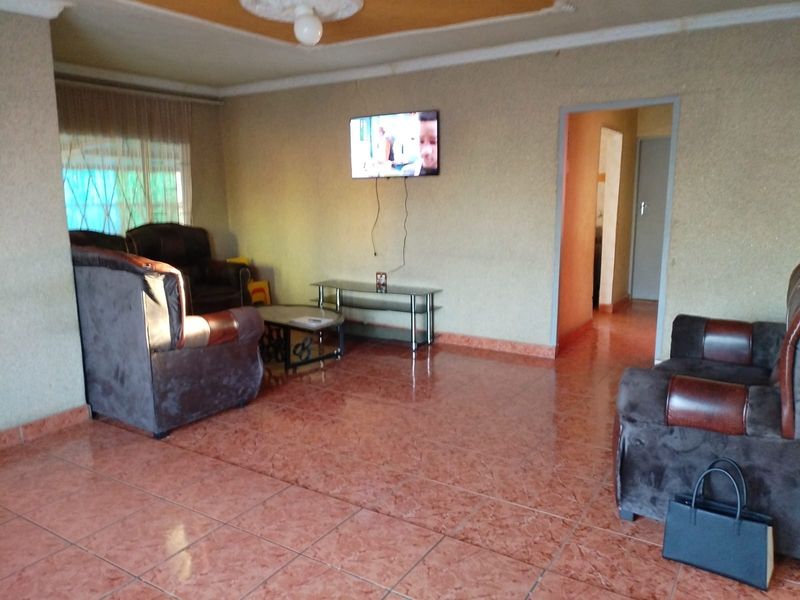 A living room featuring tiled flooring, coved ceilings with a central rose, and access to an adjacent hallway.