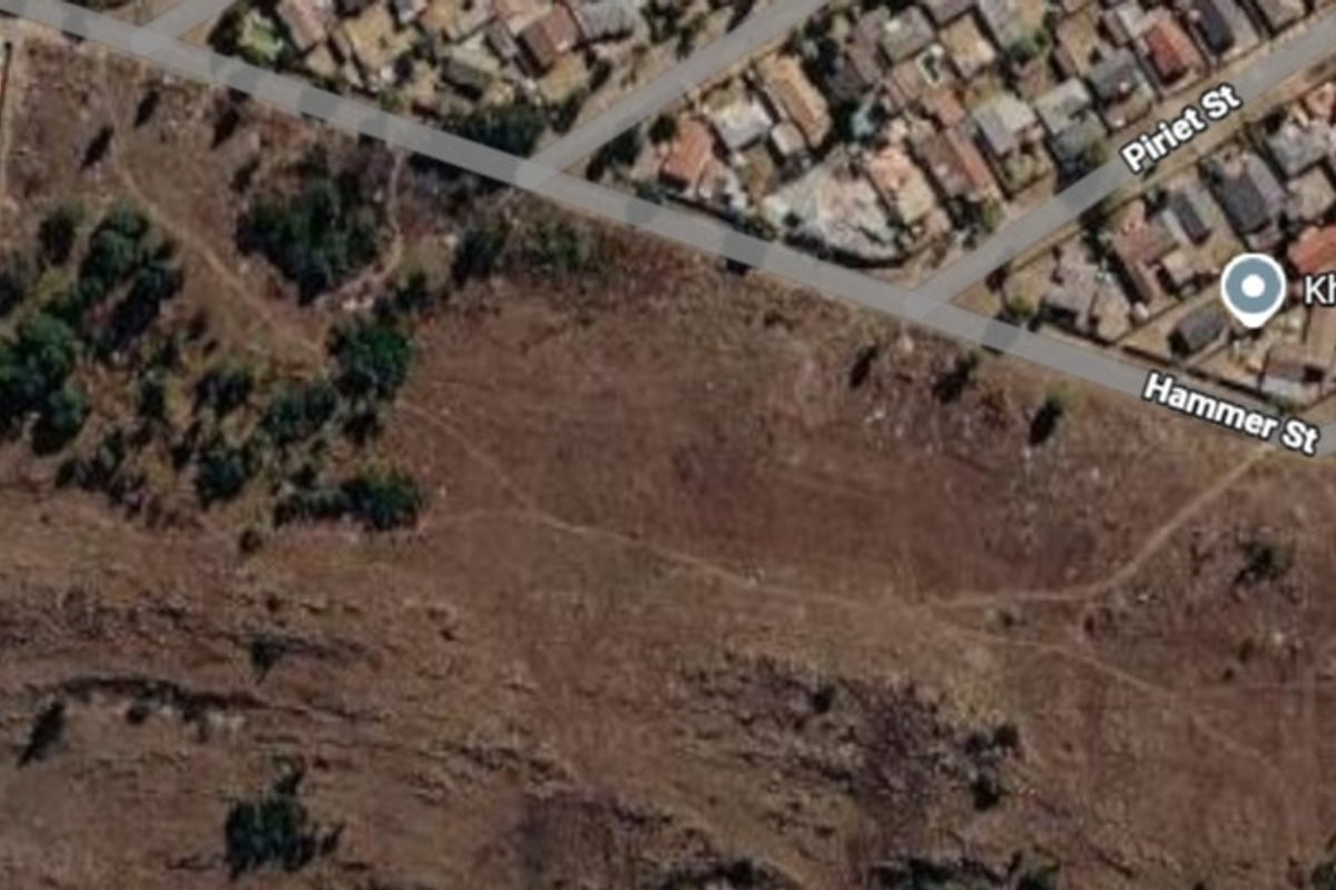 An aerial view of a large, undeveloped residential plot of land situated near existing suburban housing and street infrastructure.