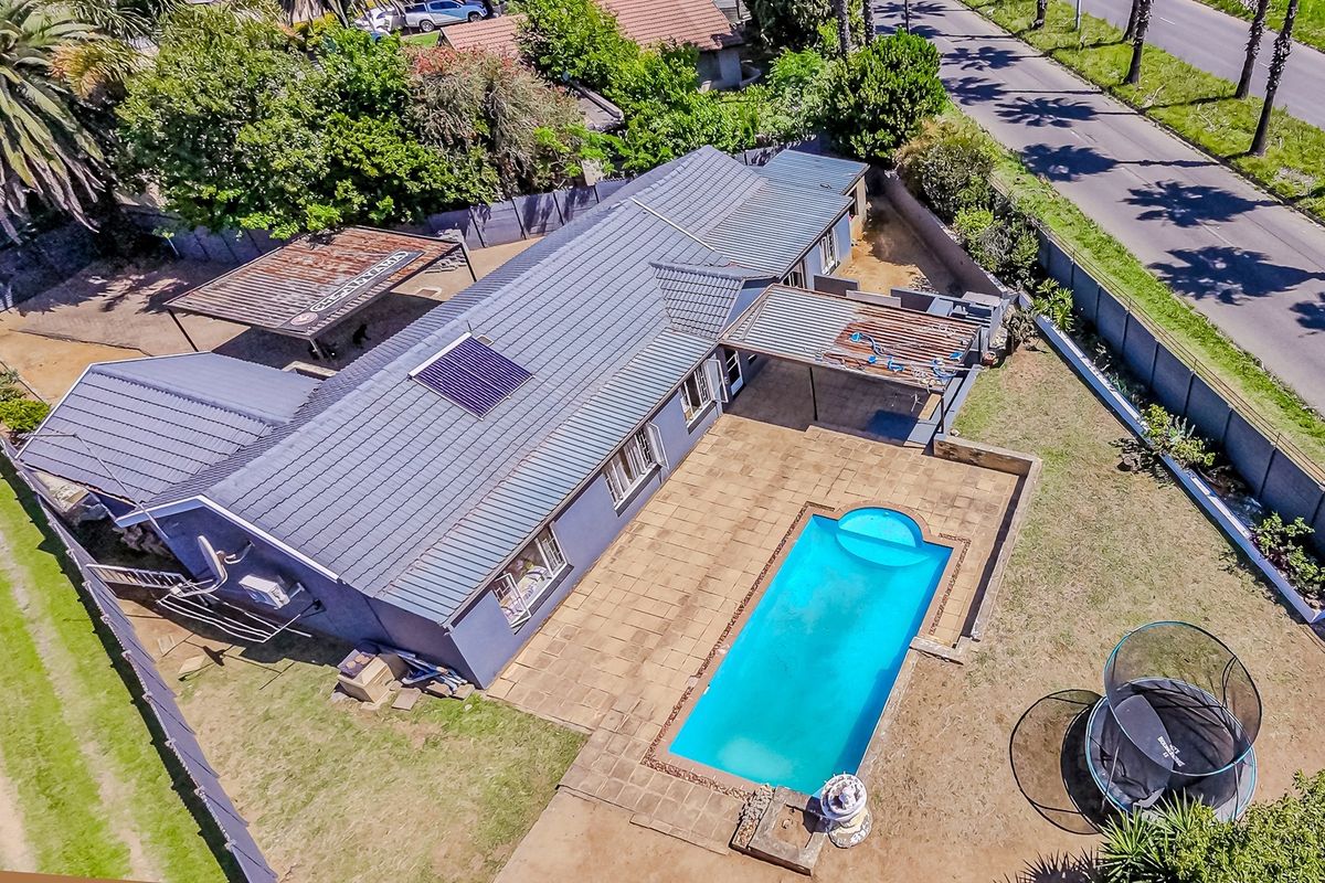 Aerial view of a residential property featuring a tiled roof with solar panel, swimming pool, paved patio area, and a carport.