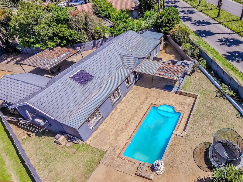 Aerial view of a residential property featuring a tiled roof with solar panel, swimming pool, paved patio area, and a carport.