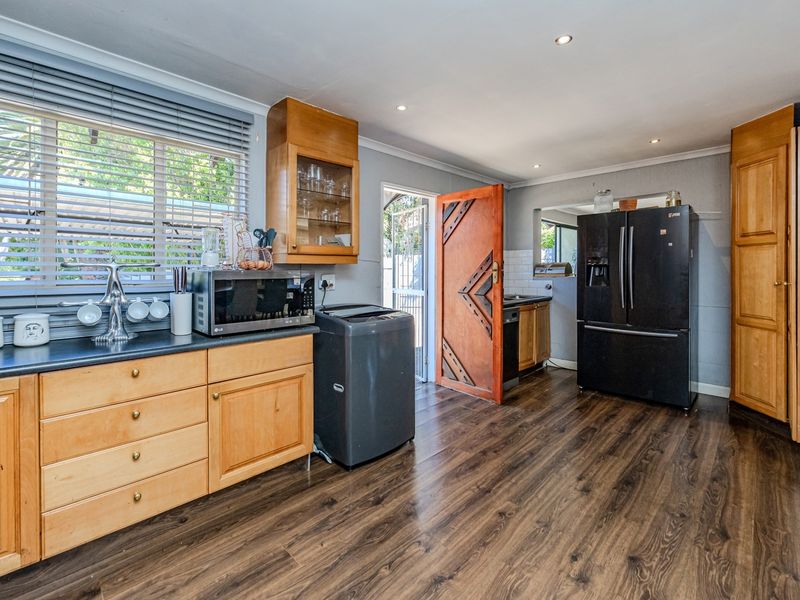 A functional kitchen featuring wooden cabinetry, laminate countertops, and durable laminate flooring, with direct access to an exterior door.