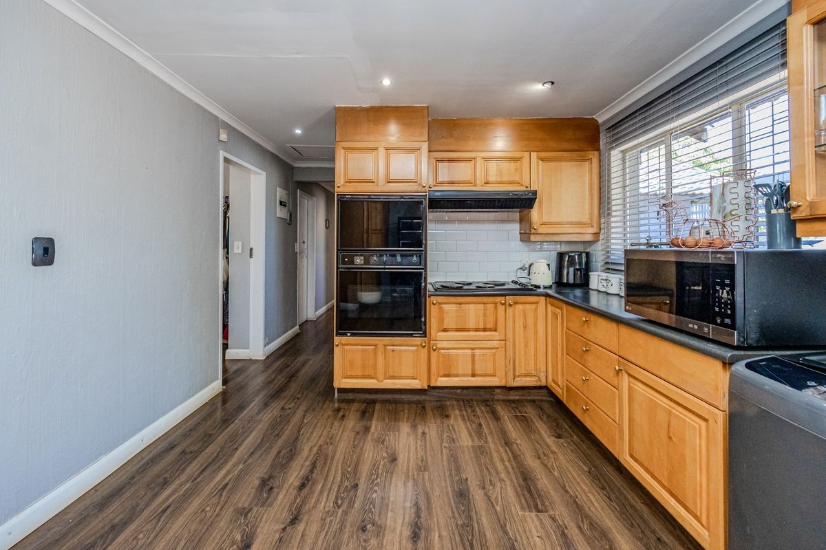 A functional kitchen featuring wooden cabinetry, integrated double oven, electric hob, and subway tile backsplash with durable laminate flooring.