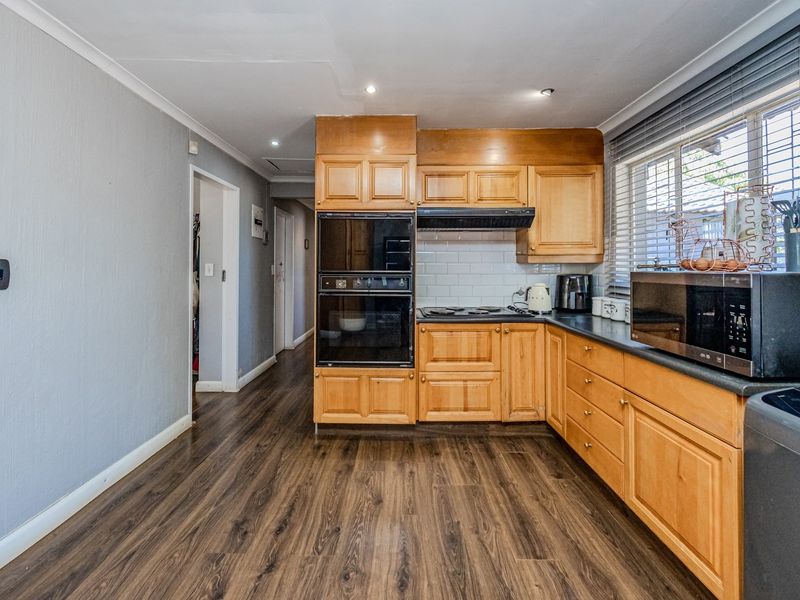 A functional kitchen featuring wooden cabinetry, integrated double oven, electric hob, and subway tile backsplash with durable laminate flooring.