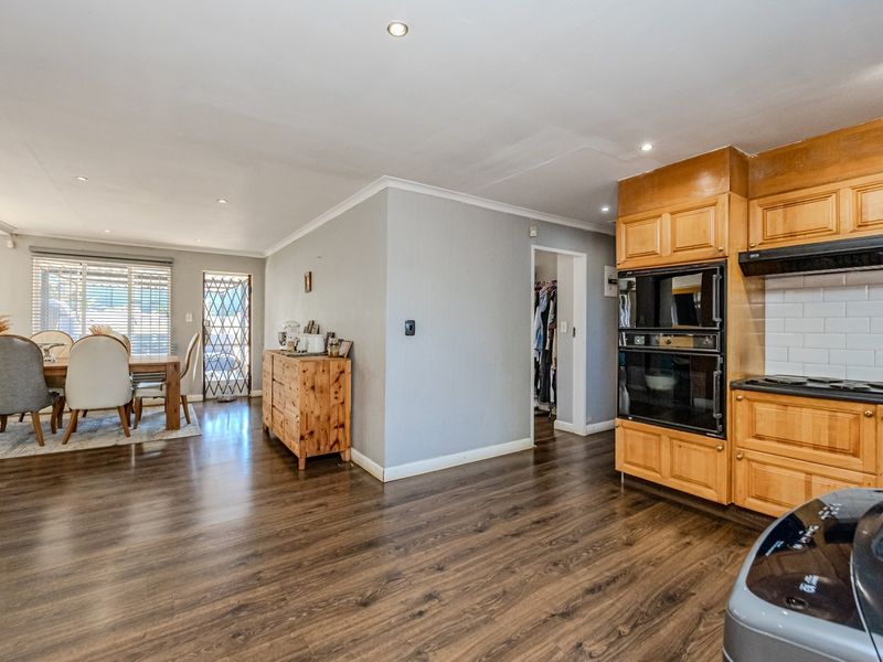 Open-plan kitchen and dining area featuring wooden cabinetry, built-in oven, hob, extractor fan, and laminate flooring throughout.