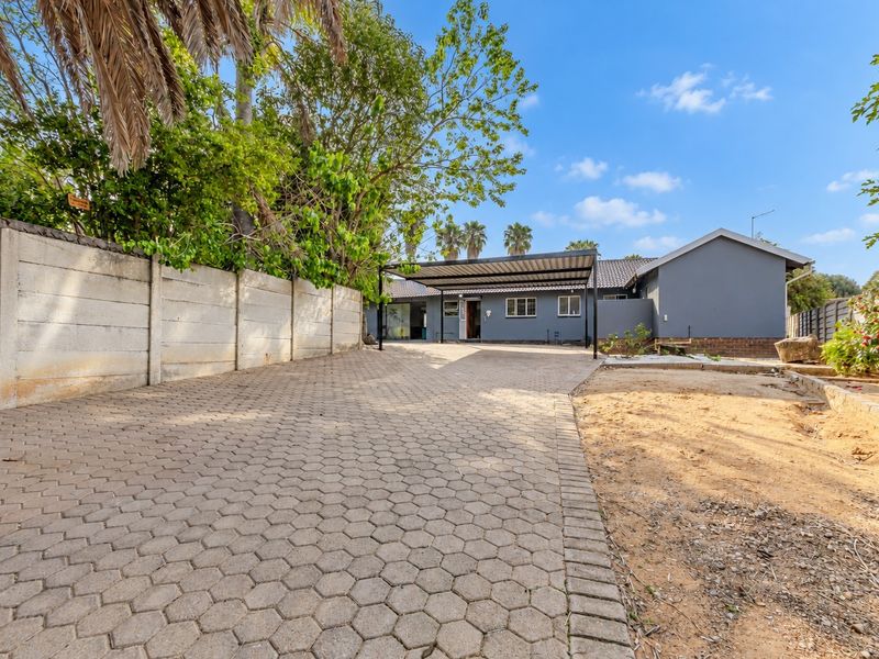 Front exterior view featuring a paved driveway, covered carport, and a grey-painted house facade with a precast concrete boundary wall.