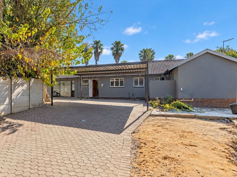 Front exterior view of the house featuring a paved driveway, a covered carport, and a neutral grey facade with a tiled roof.