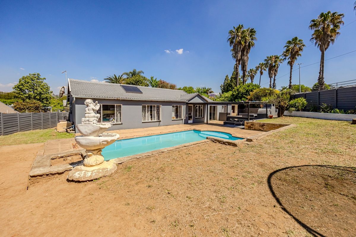 Rear exterior view of the house featuring a swimming pool, paved patio area, and a landscaped garden with a water feature.