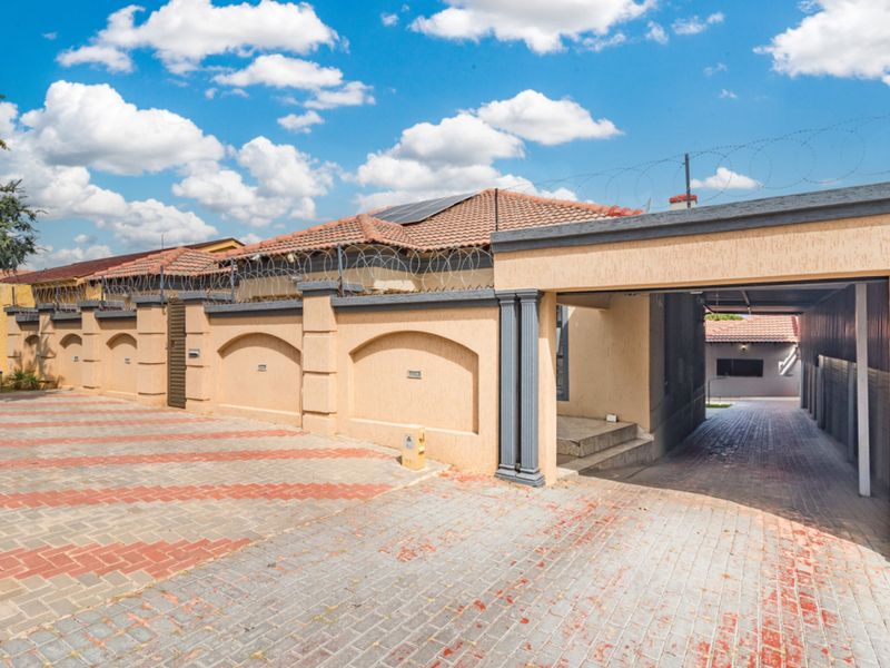 Front exterior view featuring a paved driveway, secure perimeter wall with razor wire, and a covered carport area.