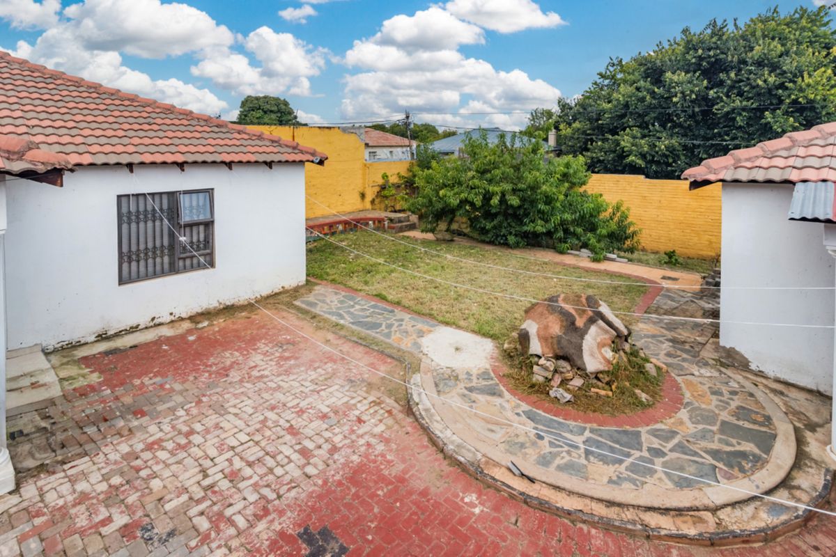 A rear courtyard area featuring a mix of paved surfaces, a small lawn, and perimeter boundary walls with a tiled roof structure.