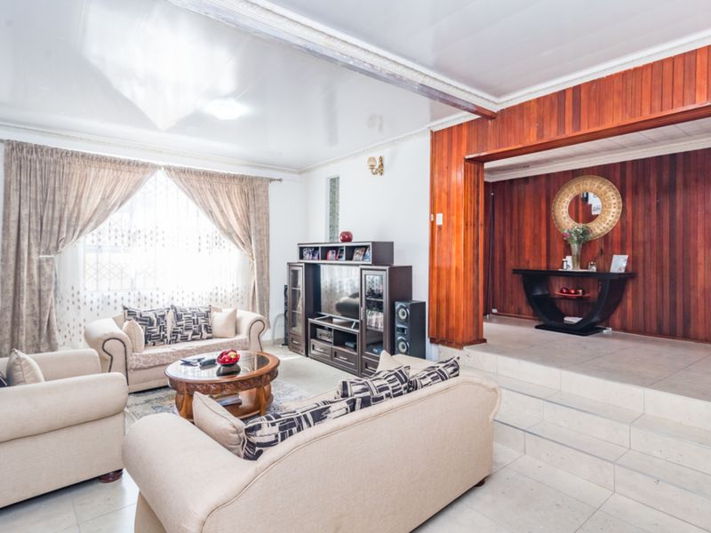 Spacious living room featuring tiled flooring, wood-paneled accent walls, and a raised platform area, offering a distinct layout with classic architectural details.