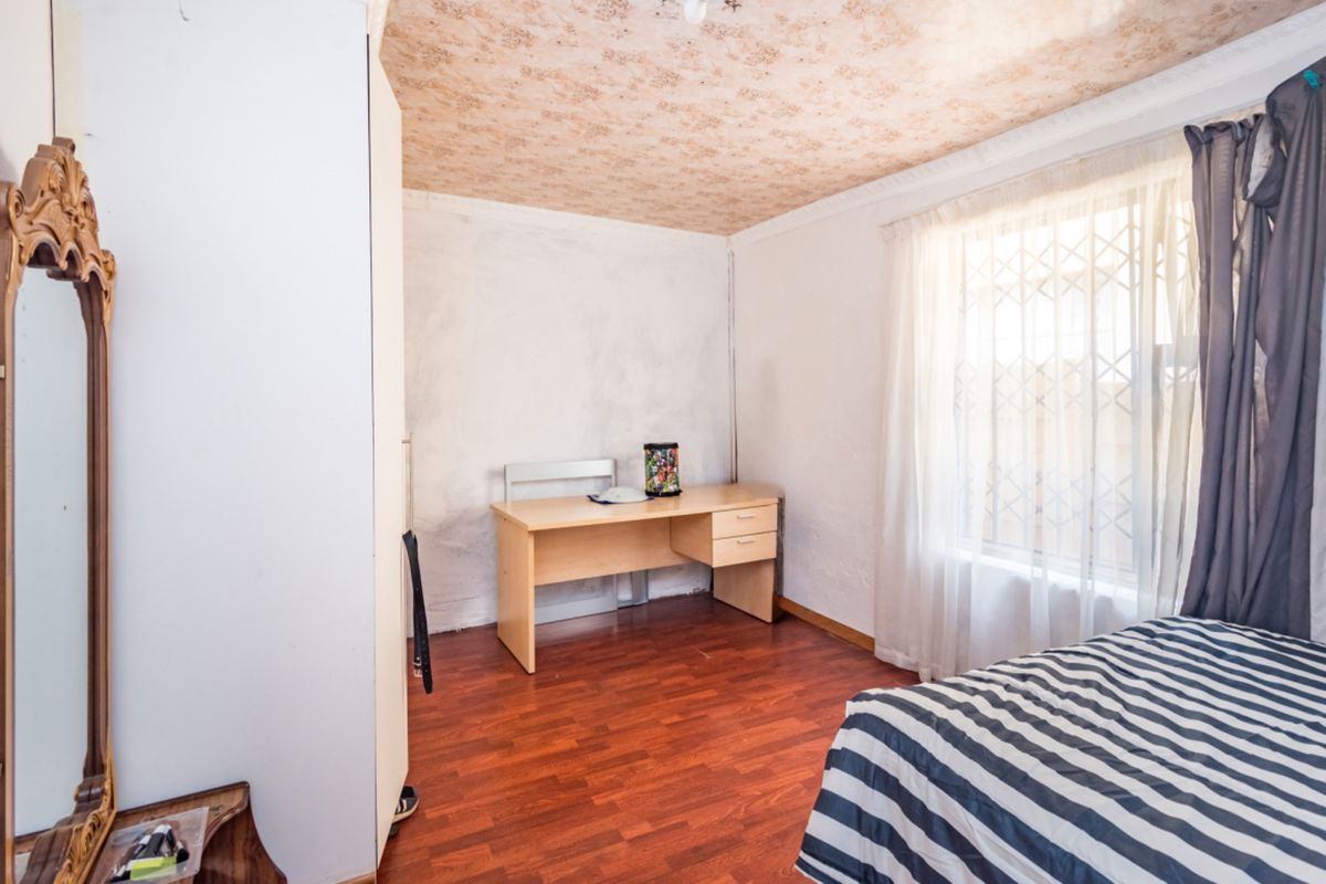 A bedroom featuring laminate flooring, a built-in wardrobe, and a window with a security gate. The ceiling requires cosmetic attention.