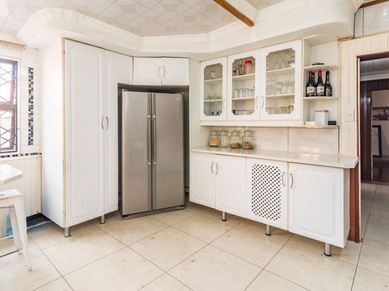 A functional kitchen featuring white built-in cabinetry, glass display units, tiled flooring, and security bars on the window.