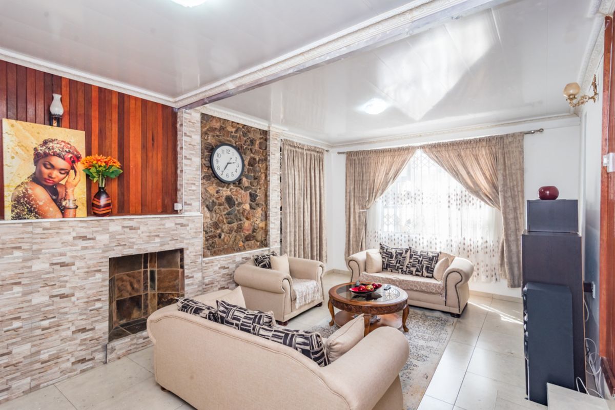 A living room featuring a stone fireplace, wood-paneled accent wall, tiled flooring, and decorative ceiling molding.