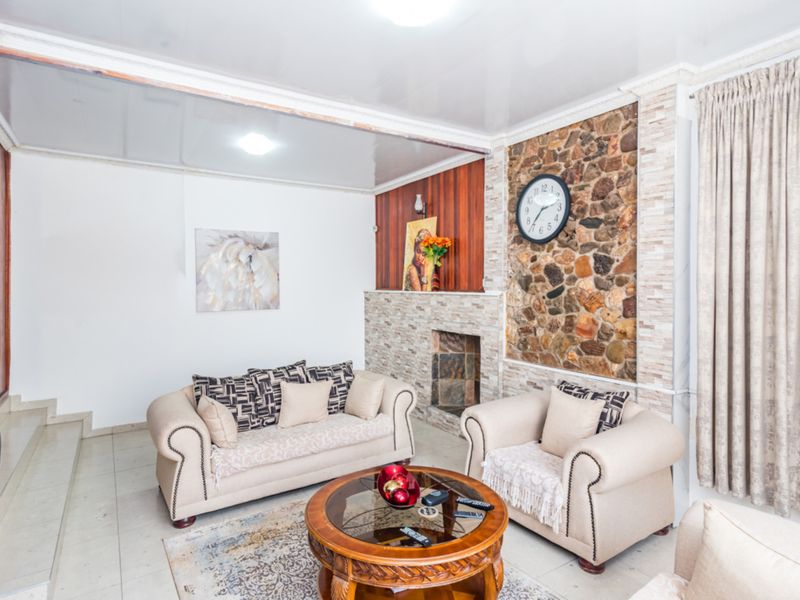 A living room featuring a prominent stone accent wall with a built-in fireplace, tiled flooring, and wood paneling details.