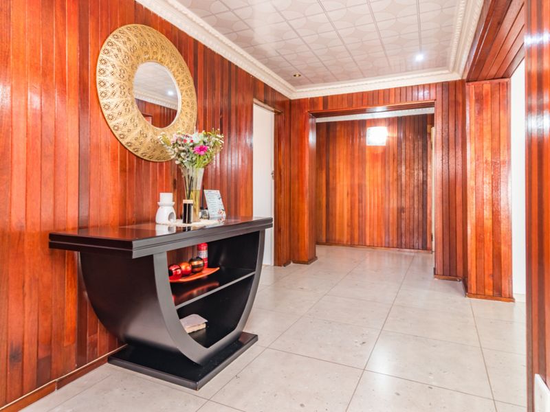 A spacious hallway featuring extensive timber wall paneling, tiled flooring, and decorative ceiling tiles, creating a warm and traditional entrance area.