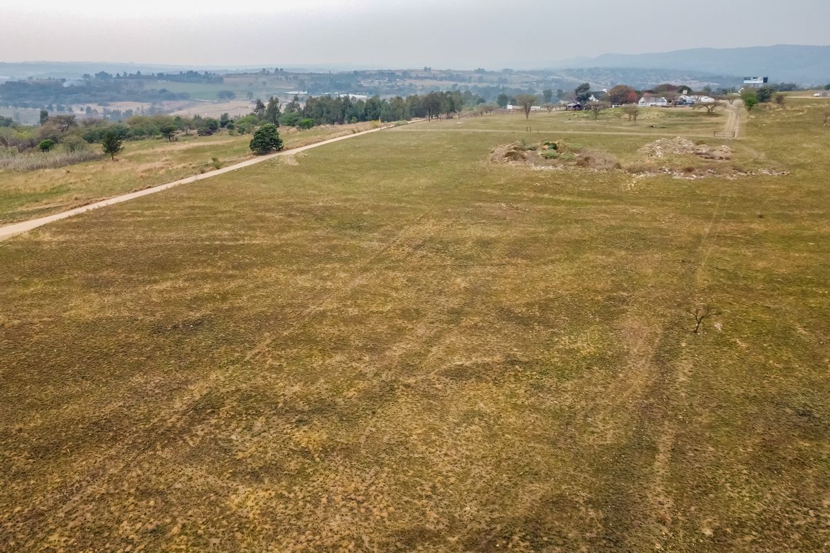 An aerial view of a large, vacant residential plot featuring open grassland and a dirt access road with distant landscape views.