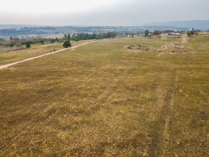 An aerial view of a large, vacant residential plot featuring open grassland and a dirt access road with distant landscape views.
