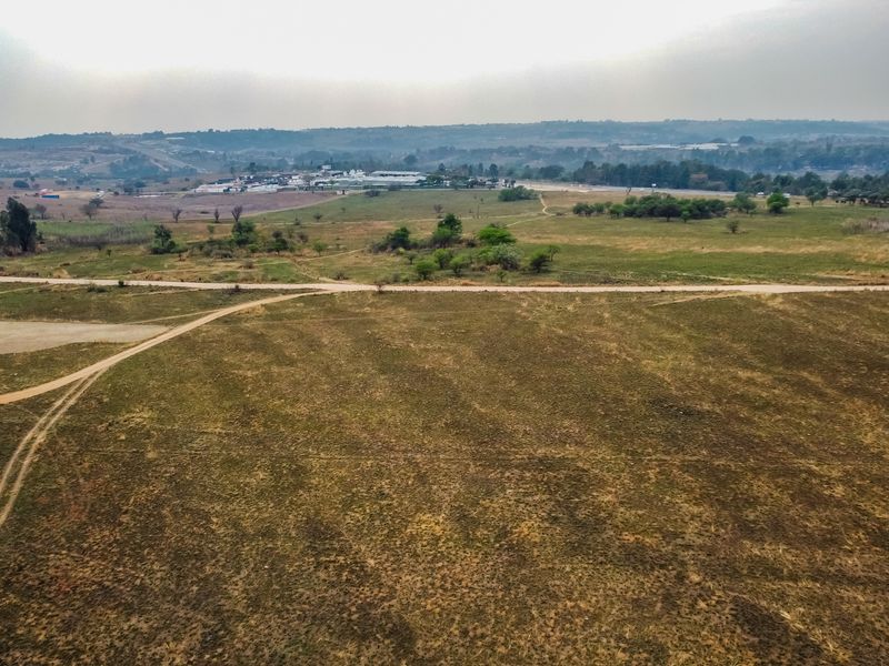 An aerial view of a large, vacant residential plot featuring natural grassland and an existing dirt access road.