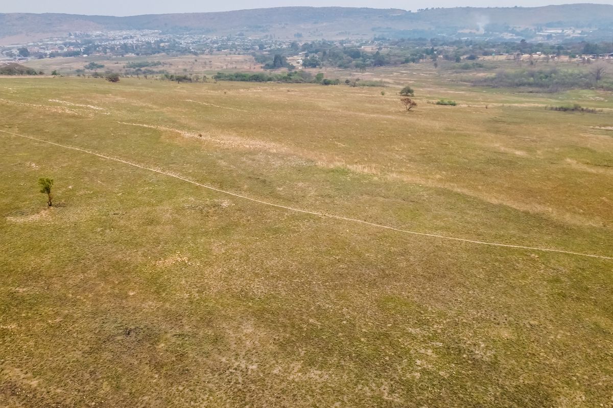An aerial view of a large, undeveloped residential plot featuring open grassland and distant landscape views.