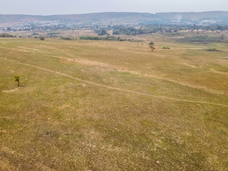 An aerial view of a large, undeveloped residential plot featuring open grassland and distant landscape views.