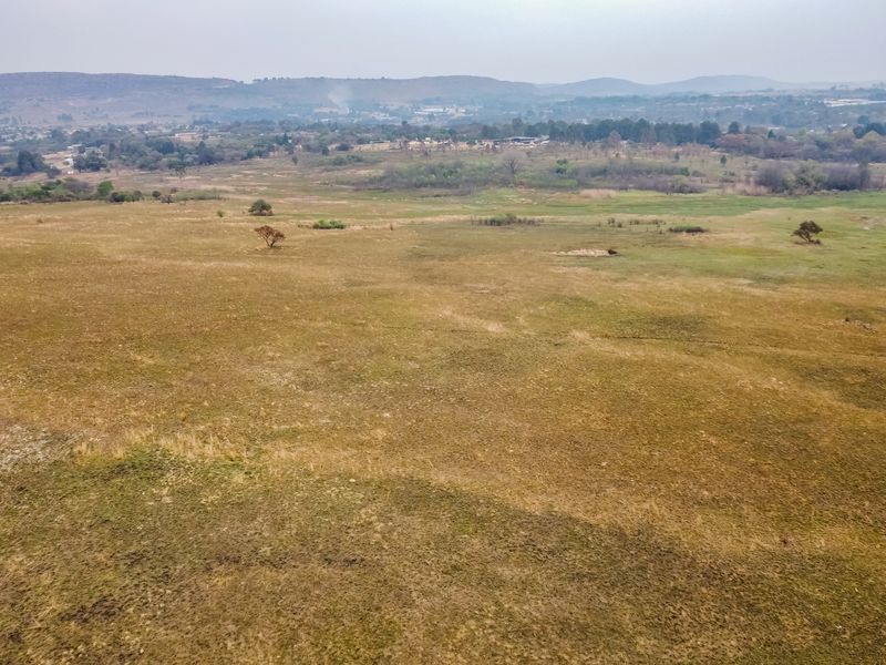 An aerial view of a large, open vacant residential plot featuring natural grassland and distant landscape views.